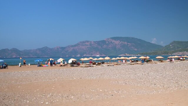 IZMIR, TURKEY - SEPTEMBER 1, 2023: Group of people enjoying relaxing beach day on patara beach, sunbathing and relaxing by sea, admiring picturesque mountain landscape on sunny day.