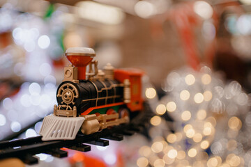 toy vintage steam locomotive on the floor under a decorated Christmas tree on a background of bokeh lights garland. Family fun, joy, activity for little kids. Children's new year holiday.