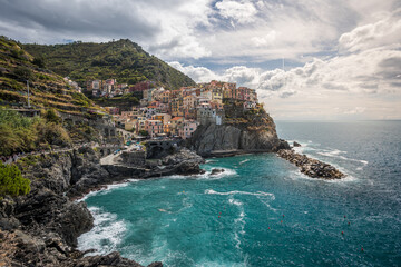 Stunning view of Manarola village in Cinque Terre National Park, beautiful cityscape with colorful houses and green terraces on cliffs over a sea, Liguria region of Italy.