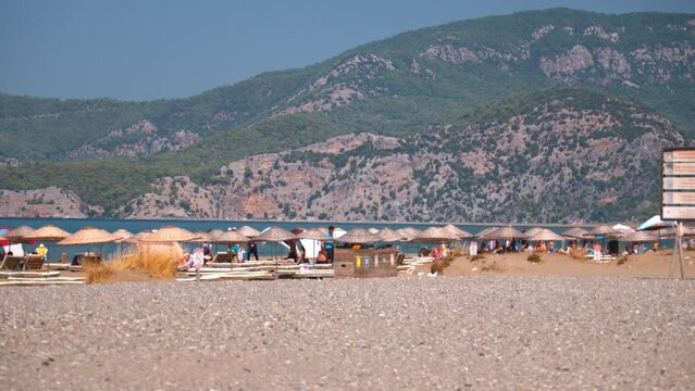 IZMIR, TURKEY - SEPTEMBER 1, 2023: Group of people enjoying relaxing beach day on patara beach, sunbathing and relaxing by sea, admiring picturesque mountain landscape on sunny day.
