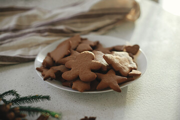 Fresh baked gingerbread cookies in plate with fir branches, pine cones and napkin on modern...