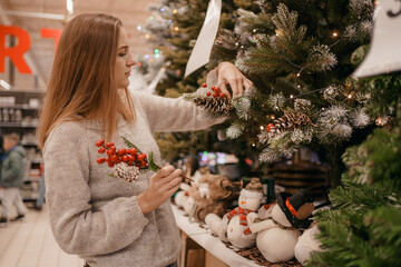 Cute young woman choosing artificial Christmas tree in Xmas store. Christmas concept store, buying...