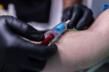 Focused photo of two hands with black gloves performing a blood draw.