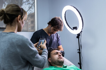 Photo of an aesthetic clinic with a doctor performing a treatment to his client and a woman is...