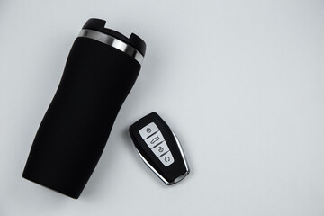 A thermocup and a key with automatic buttons in black with metal inserts lie on a white background...