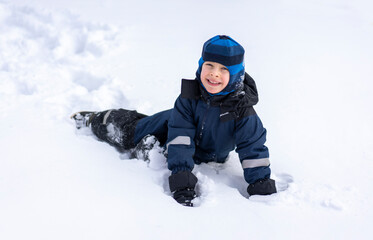 Fototapeta na wymiar A little boy lies in a snowdrift and smiles. Winter entertainment concept