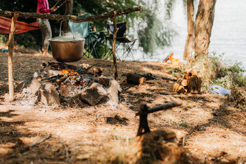 Travel a kettle over a fire burning on the river and sunset backgroun. Cooking over a campfire