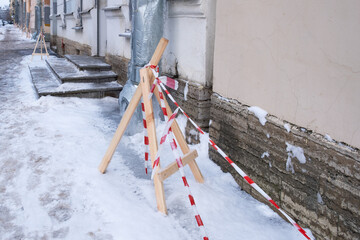 A snow-covered city sidewalk is protected from falling icicles by warning tape