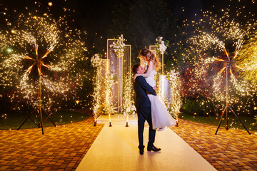 The bride and groom on the wedding ceremony venue with fireworks at night . 