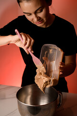 Female confectioner pours cream from a container into the bowl of a mixer