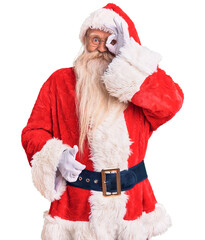 Old senior man with grey hair and long beard wearing traditional santa claus costume doing ok gesture with hand smiling, eye looking through fingers with happy face.