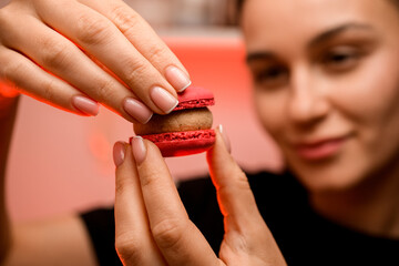 Confectioner holds two halves of red macaroon with beige cream together, close up