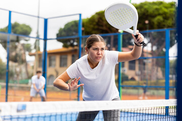 Portrait of emotional young fit woman enjoying friendly padel tennis match at outdoors court - obrazy, fototapety, plakaty