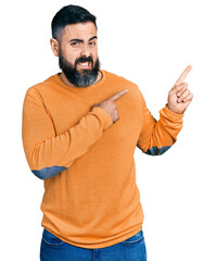 Hispanic man with beard wearing casual winter sweater pointing aside worried and nervous with both...