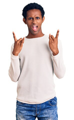 African handsome man wearing casual winter sweater shouting with crazy expression doing rock symbol with hands up. music star. heavy concept.