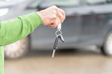 A businessman hands over a car key to a woman in front of a blurred car