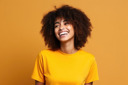 A woman with curly hair is wearing a yellow shirt and smiling