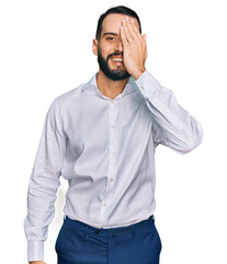 Fototapeta premium Young man with beard wearing business shirt covering one eye with hand, confident smile on face and surprise emotion.