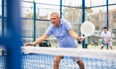 Male player ready to hits the ball while playing padel on a hard court