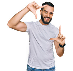 Young man with beard wearing casual white t shirt smiling making frame with hands and fingers with happy face. creativity and photography concept.