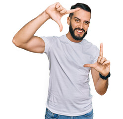 Fototapeta premium Young man with beard wearing casual white t shirt smiling making frame with hands and fingers with happy face. creativity and photography concept.