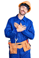 Young hispanic man wearing worker uniform smiling with hands on chest with closed eyes and grateful gesture on face. health concept.