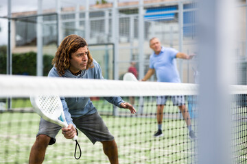 Athletic man plays padel. View through the tennis net