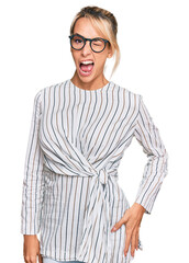 Beautiful blonde woman wearing business shirt and glasses winking looking at the camera with sexy expression, cheerful and happy face.