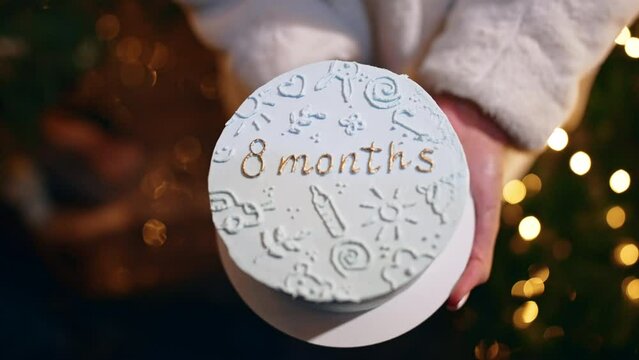 Beautiful white cake with pictures and a sign "eight months" in female hands. Celebrating the first months of child's life. Close up.