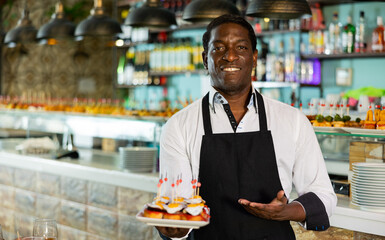 Professional friendly african american waiter holding serving tray for restaurant guests