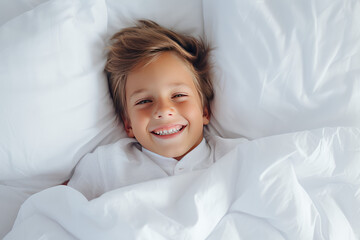 Cute happy smiling kid in bed in the morning on clean white linens. A healthy sleep routine. 