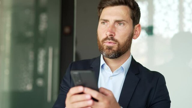 Businessman in formal suit is using smartphone at workplace in business office. Worker reads or typing message, chats with client, banking in phone app, checks email, swiping browsing online. Close up