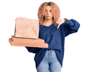 Young blonde woman with curly hair holding delivery food with angry face, negative sign showing dislike with thumbs down, rejection concept