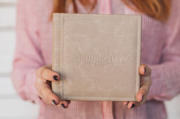 Female hands holding square photo book for wedding album. Wedding photo book, family album. Photo books with embossing and a cover of genuine leather. A book in an expensive binding. - obrazy, fototapety, plakaty