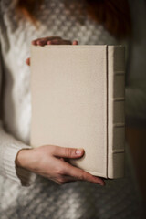 Female hands holding square photo book for wedding album. Wedding photo book, family album. Photo books with fabric cover. A book in an expensive binding.