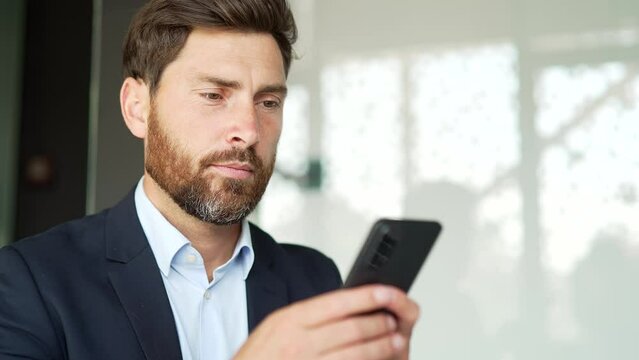 Businessman in formal suit is using smartphone at workplace in business office. Worker reads or typing message, chats with client, banking in a mobile phone app, checks email, browsing online Close up