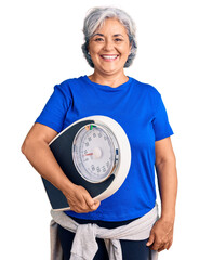 Senior woman with gray hair holding weight machine to balance weight loss looking positive and...