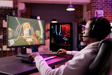 Man in brick wall living room playing engaging video games on gaming PC at computer desk, chilling after work. Gamer contending against foes in online multiplayer shooter