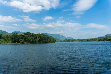 Fototapeta na wymiar Beautiful lakeside view from a small lake in Kanchanaburi Thailand, with green trees, blue sky and sunlight