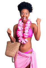 Young african american woman wearing bikini and hawaiian lei screaming proud, celebrating victory and success very excited with raised arms