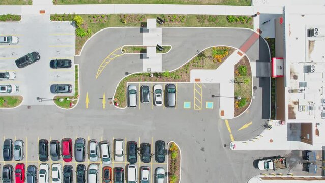 Aerial, bird eye perspective of a grocery store plaza, supermarket, or shopping mall parking area, where numerous vehicles are constantly entering and exiting, captured in a time-lapse or hyper-lapse.