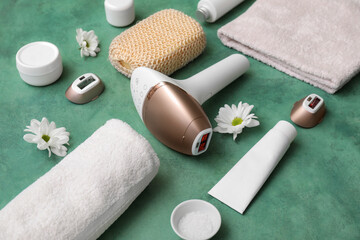 Modern photoepilator with cosmetic products, bath supplies and camomile flowers on grunge green background