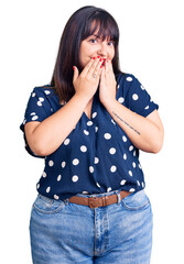Young plus size woman wearing casual clothes laughing and embarrassed giggle covering mouth with...