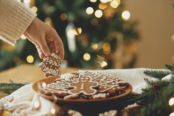 Merry Christmas! Hand holding gingerbread cookie with icing on background of cookies in plate on...