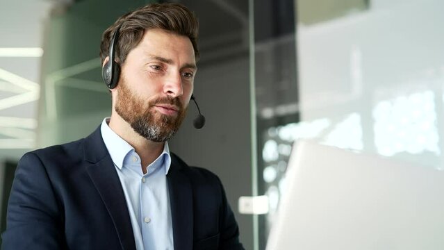A corporate operator who works in customer support speaks on a video call using a laptop. Call center agent in wireless headset helping clients with complaints in office. Online consultation. Close up