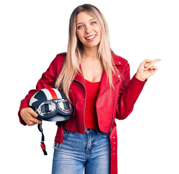 Young beautiful blonde woman holding motorcycle helmet smiling happy pointing with hand and finger to the side