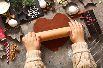 Woman rolling out gingerbread dough for Christmas cookies on grunge grey background