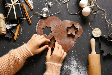 Woman preparing tasty Christmas gingerbread cookies on black background
