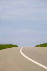 Asphalt road with green grass and blue sky in the background.