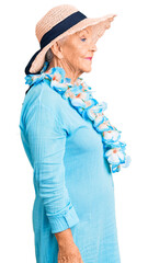 Senior beautiful woman with blue eyes and grey hair wearing summer hat and hawaiian lei looking to...